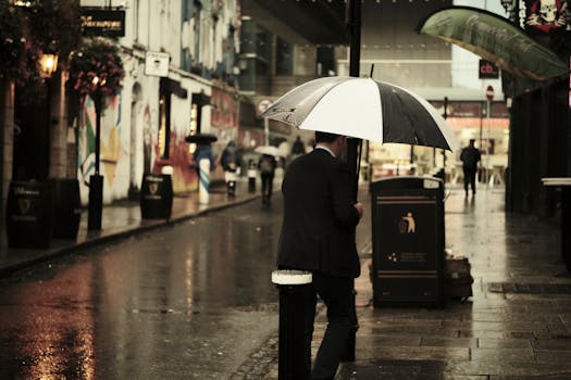 Moody street photo capturing a man with an umbrella in a city after rain.