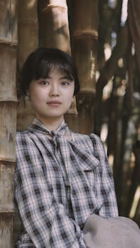 A serene portrait of a young woman standing amidst bamboo trees, capturing a tranquil moment in nature.