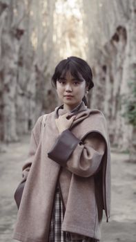 A young woman poses in a stylish coat on a serene forest path, exuding elegance.