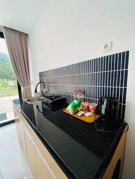 Contemporary kitchenette with cooker, kettle, and snacks by a window.