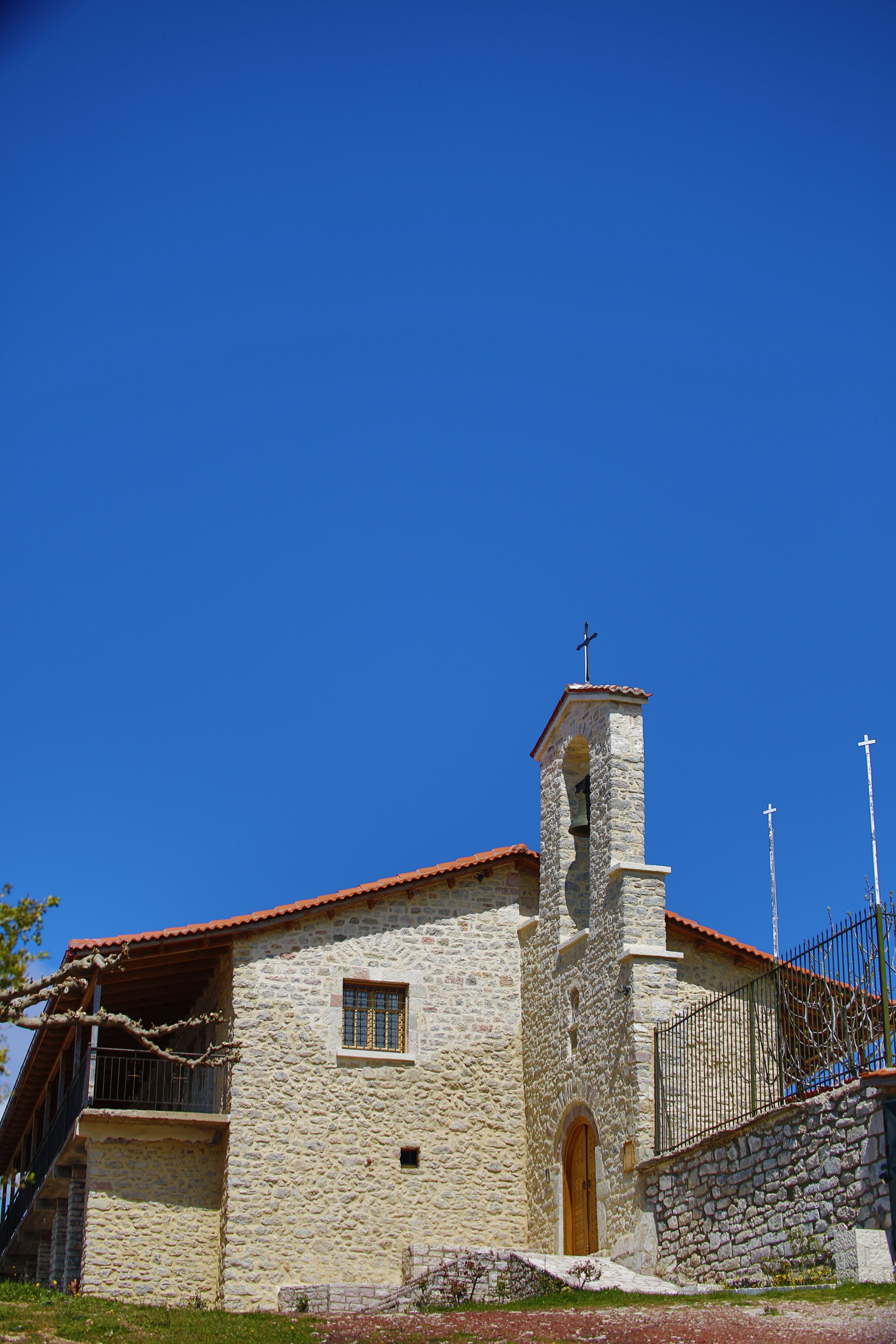 A quaint stone church with a red tile roof stands against a clear blue sky.