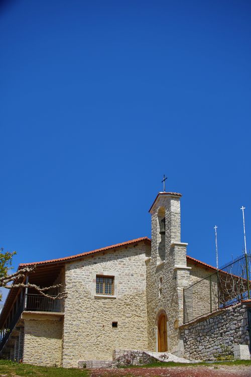 Free A quaint stone church with a red tile roof stands against a clear blue sky. Stock Photo