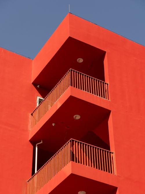 Free A striking red building with balconies stands out against a bright blue sky. Stock Photo