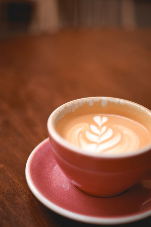 Free Close-up of a latte with latte art in a rustic pink mug on a wooden table. Stock Photo