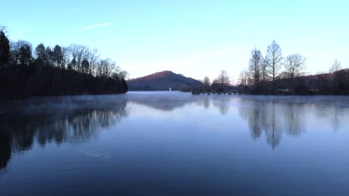 Free A serene morning scene at a foggy lake in Tennessee with a wooden dock and calm waters under a blue sky. Stock Photo