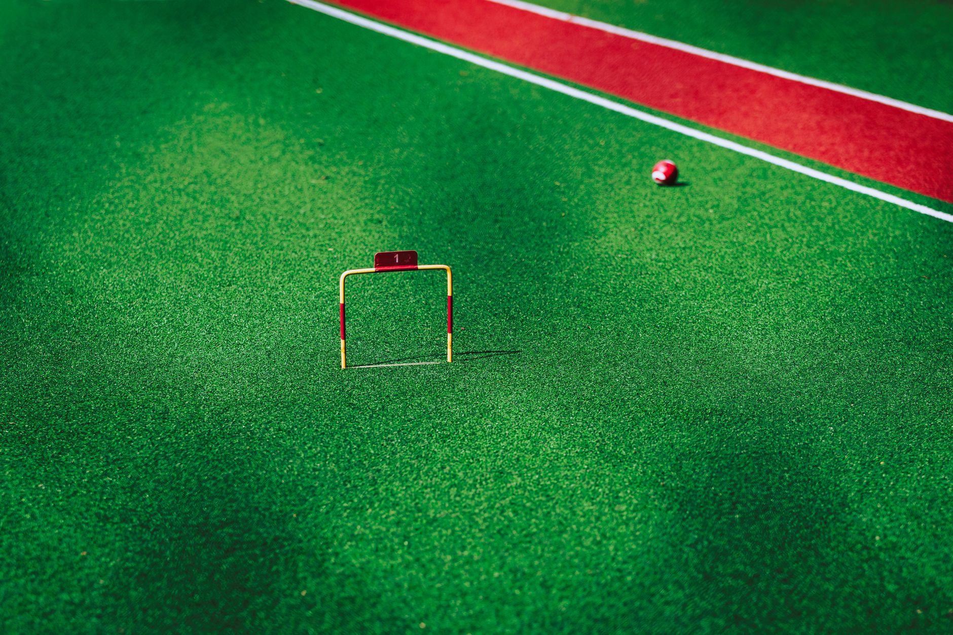 A vivid image of a gateball court showcasing a ball near the hoop on green artificial turf.