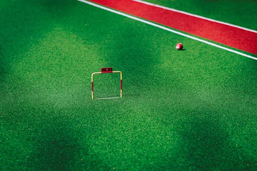 A vivid image of a gateball court showcasing a ball near the hoop on green artificial turf.