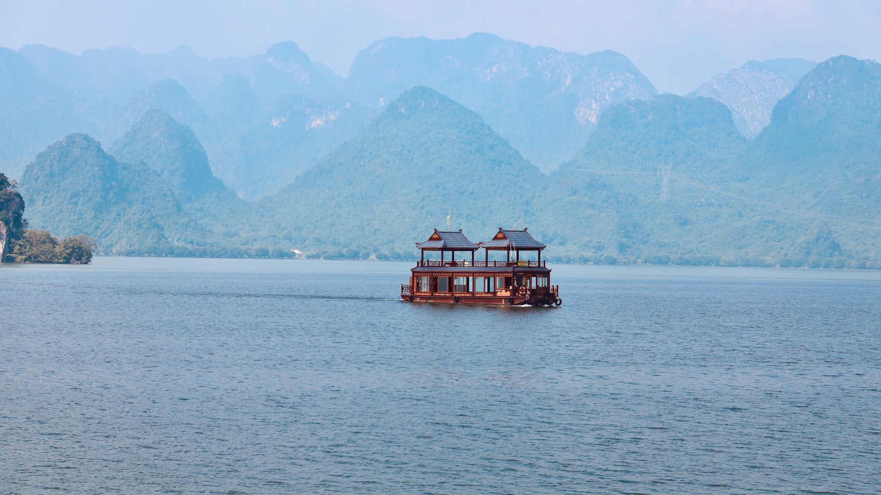 Traditional houseboat on tranquil Tam Chúc Lake against karst mountains in Hà Nam, Vietnam.