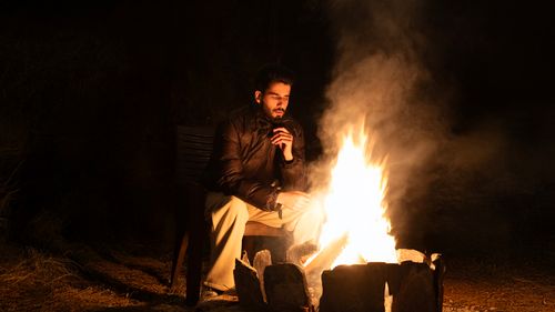 Free A man in winter attire sitting by a warm campfire at night outdoors. Stock Photo