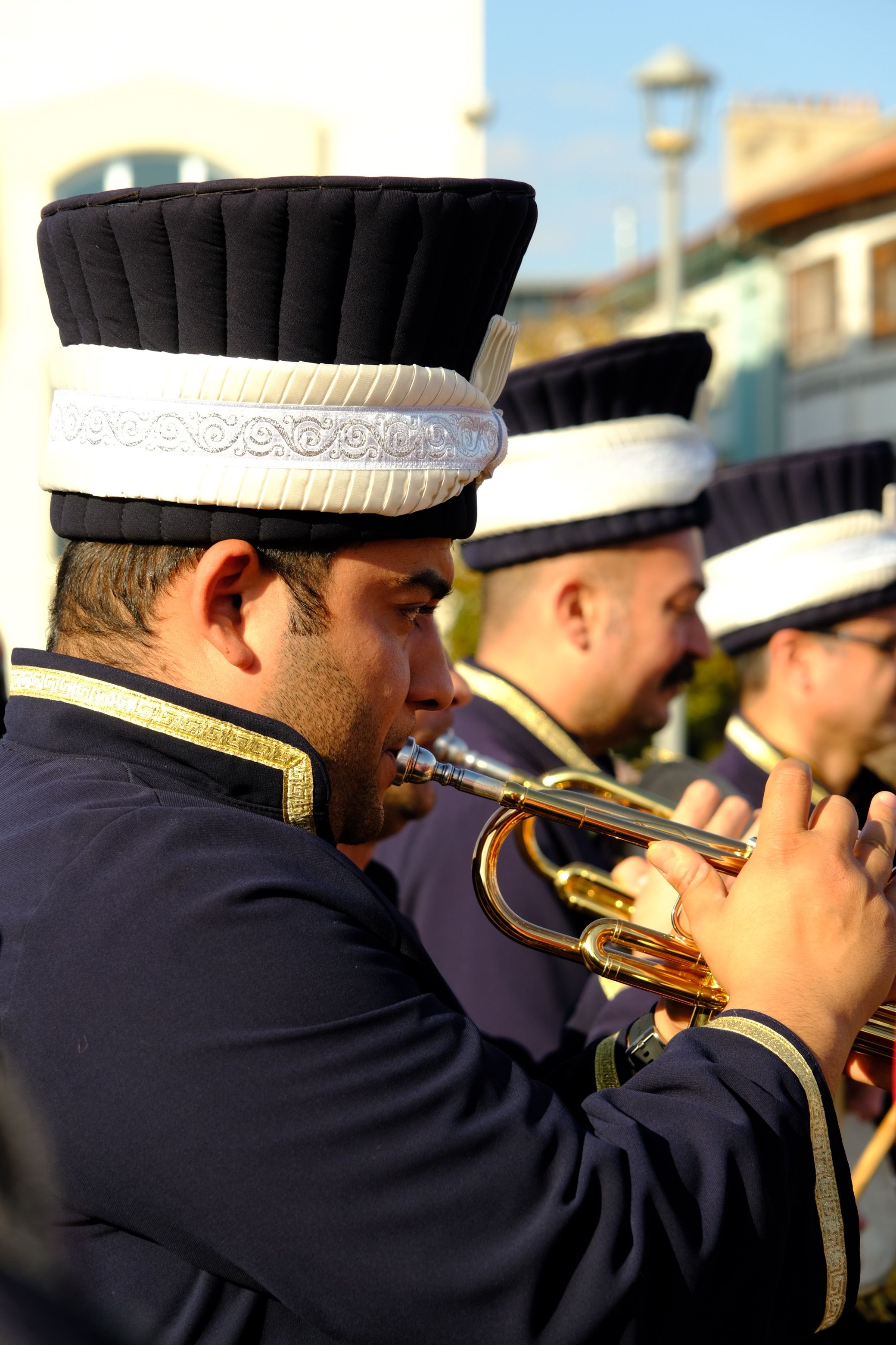 Close-up of brass band performers in uniform playing instruments during daylight.