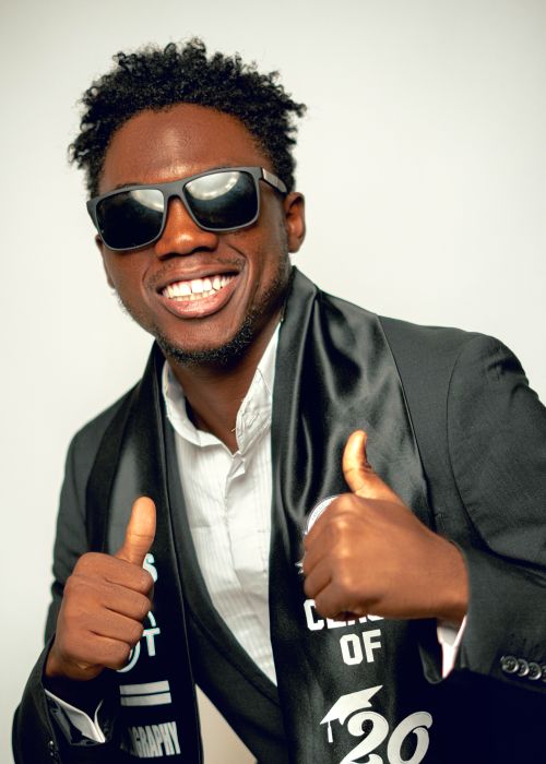 Free Smiling graduate in sunglasses celebrating success with thumbs up. Stock Photo