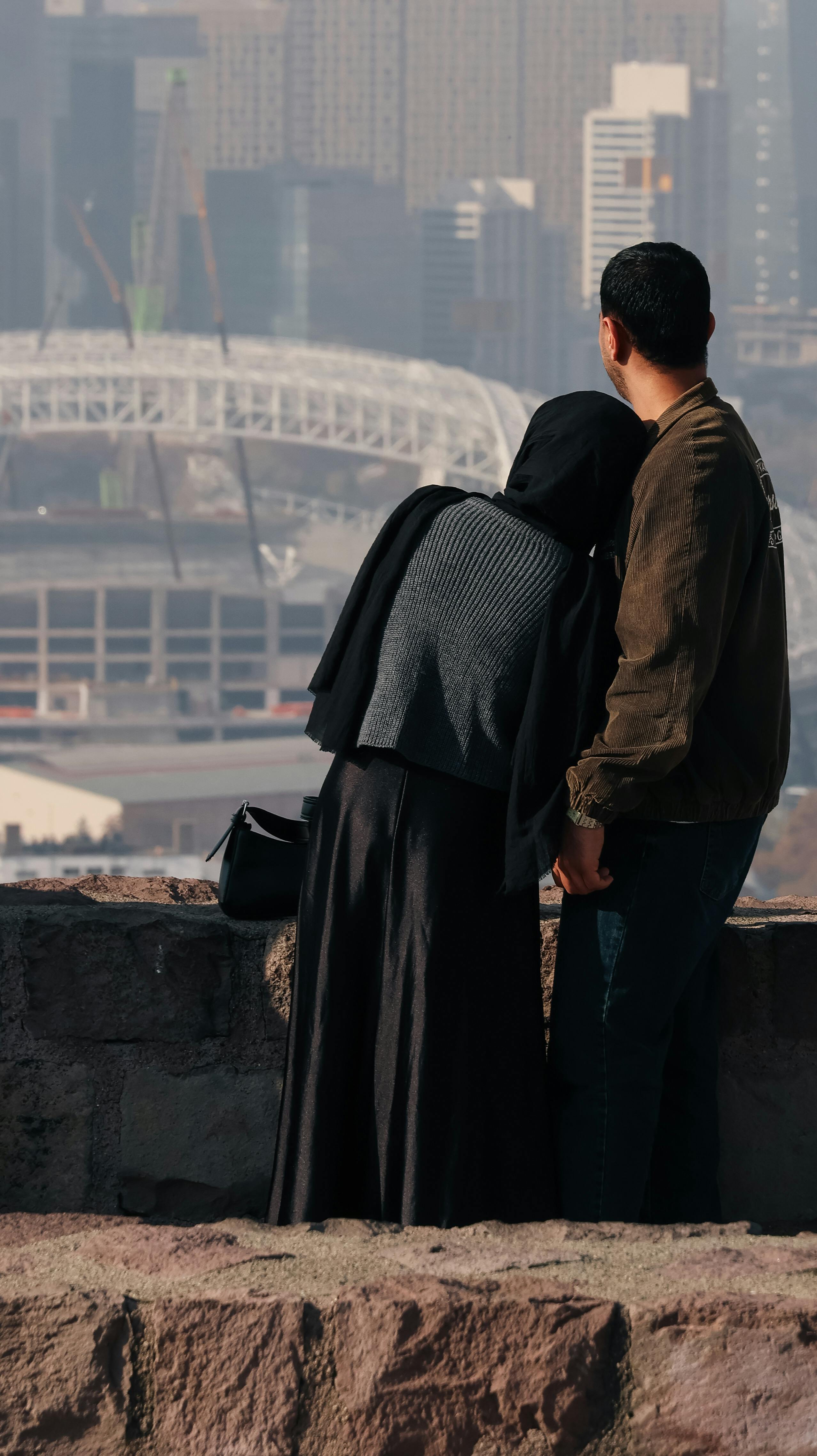 A couple enjoying the view from a balcony, overlooking an urban cityscape with a stadium in the background.
