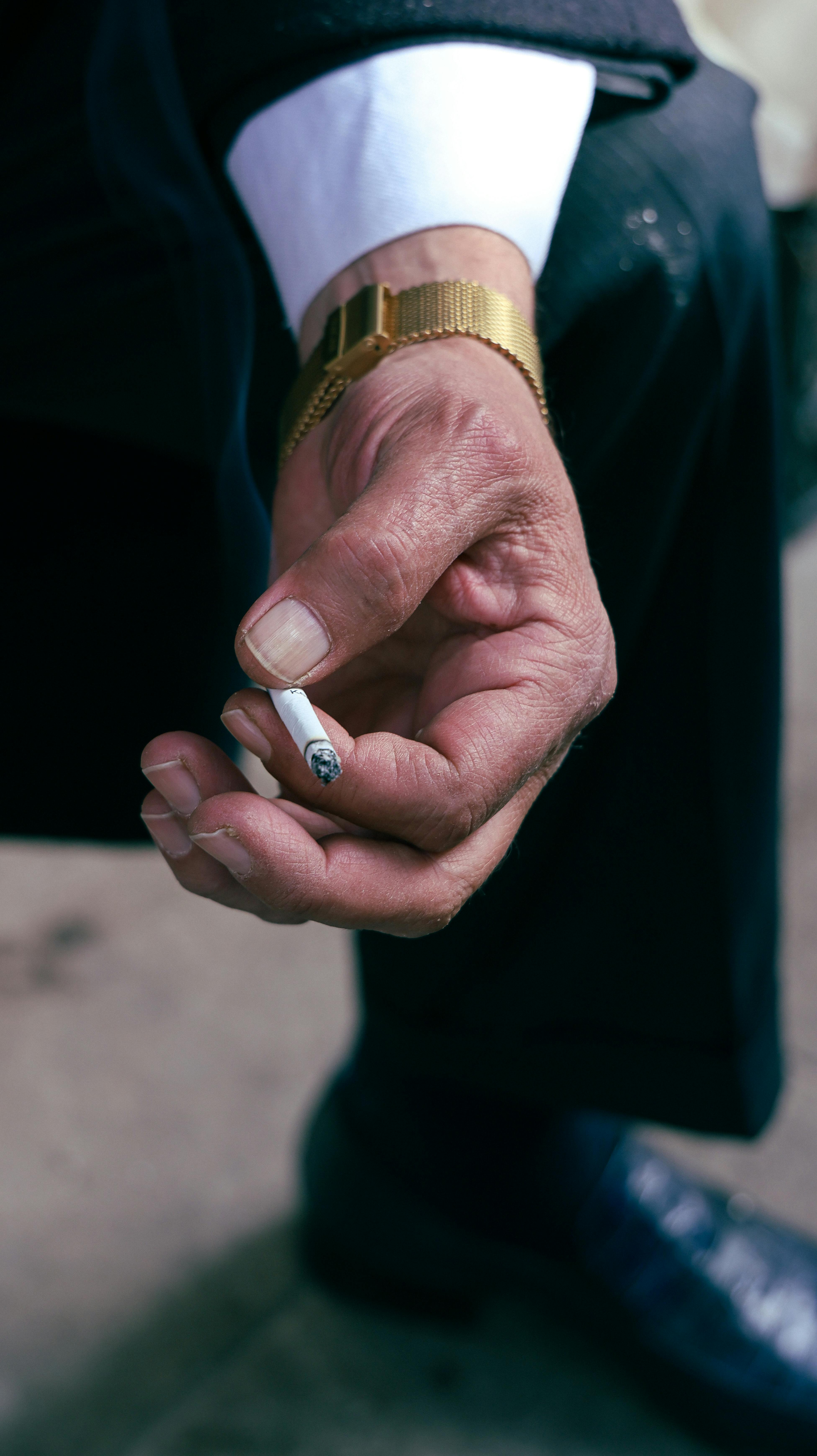 無料 金時計をはめた大人の手がタバコを握っているクローズアップ。喫煙のコンセプト。 写真素材