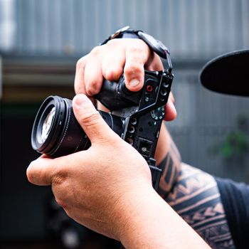 Close-up shot of hands holding a camera, showcasing tattoos and capturing a candid moment.