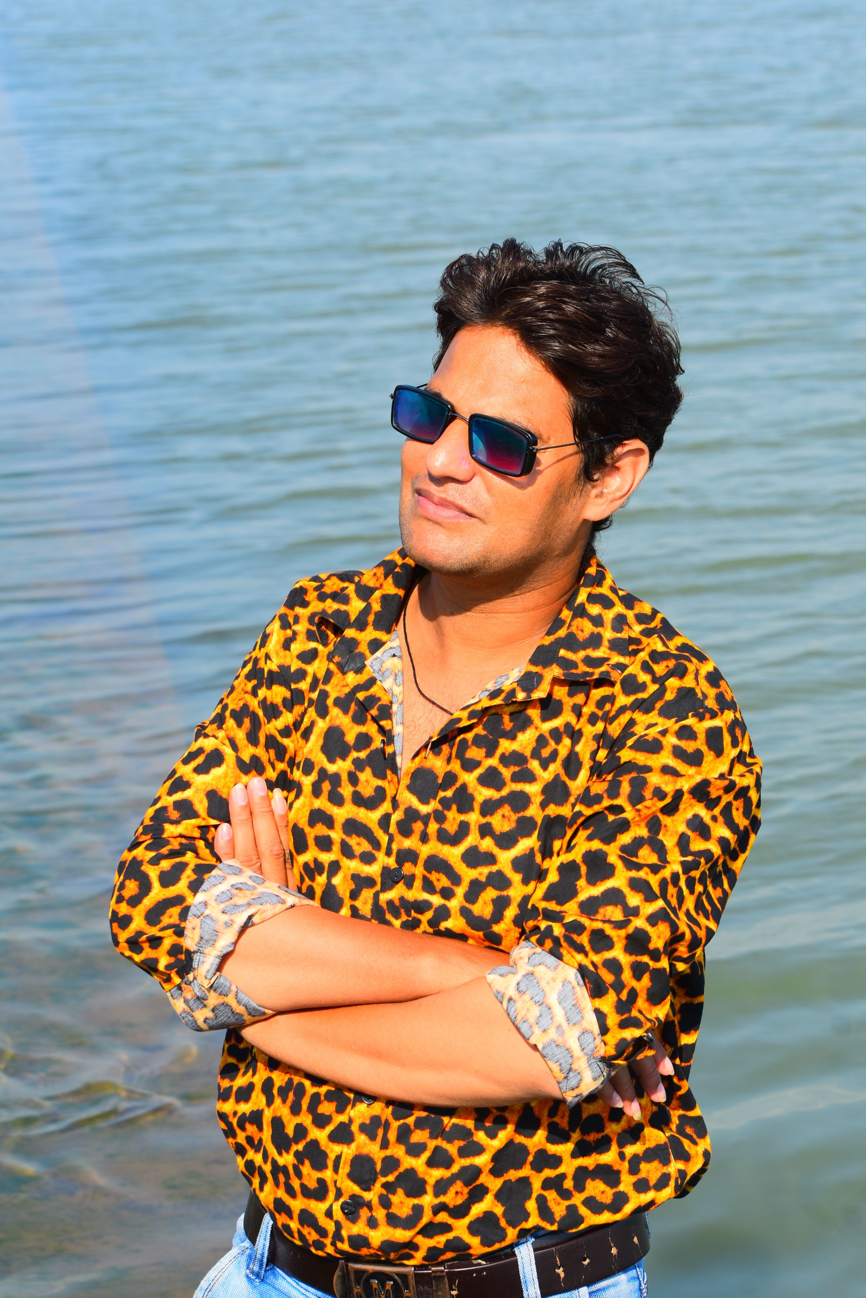 Man in leopard print shirt poses confidently by the water on a sunny day.