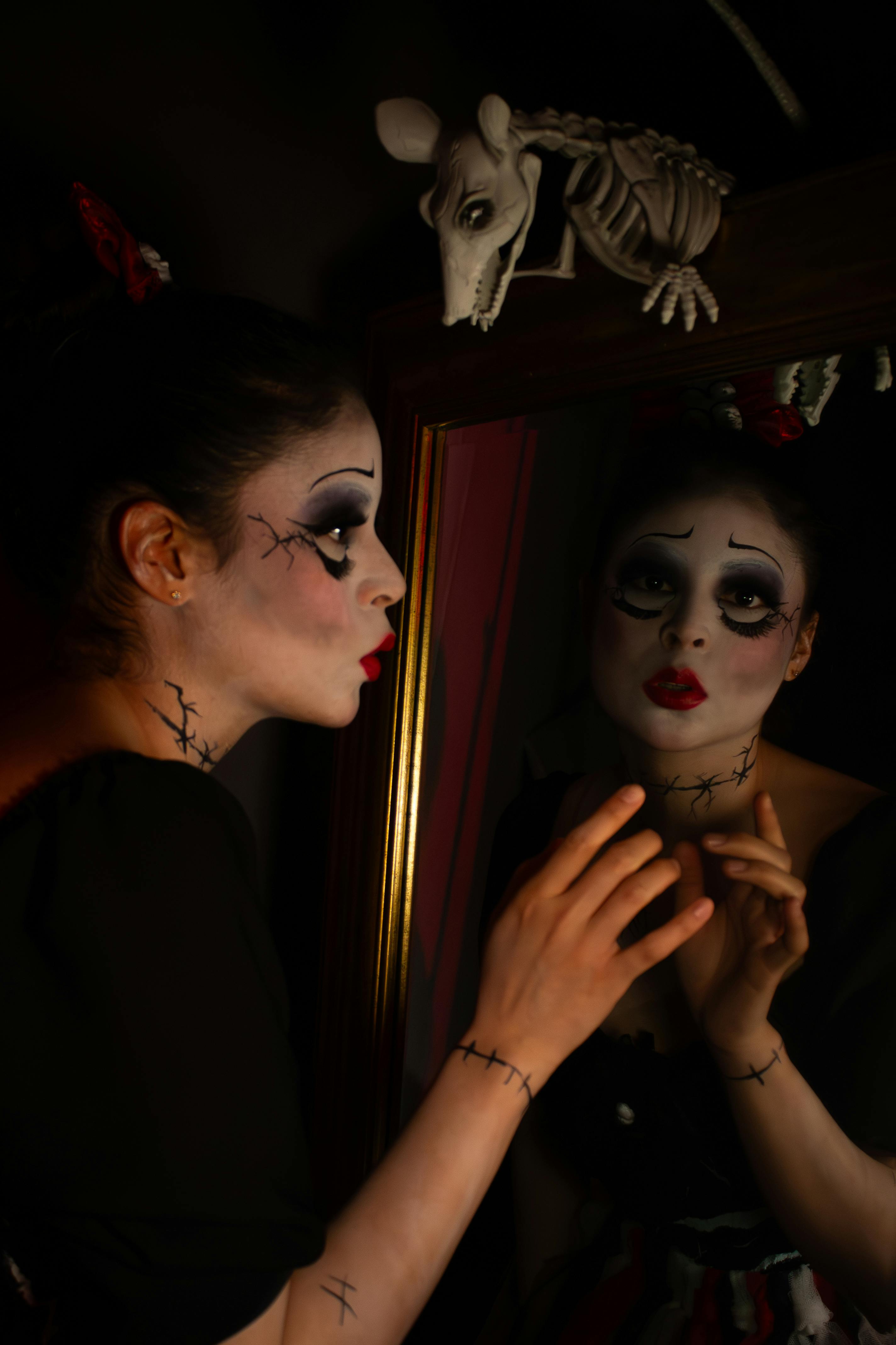 Ücretsiz Tiyatro makyajlı bir kadın aynanın önünde dramatik bir poz vererek kasvetli, karanlık bir atmosfer yaratıyor. Stok Fotoğraflar