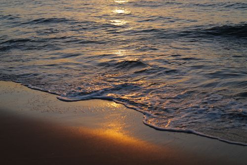 Free Serene sunset over gentle ocean waves lapping on the sandy beach, creating a tranquil and warm atmosphere. Stock Photo