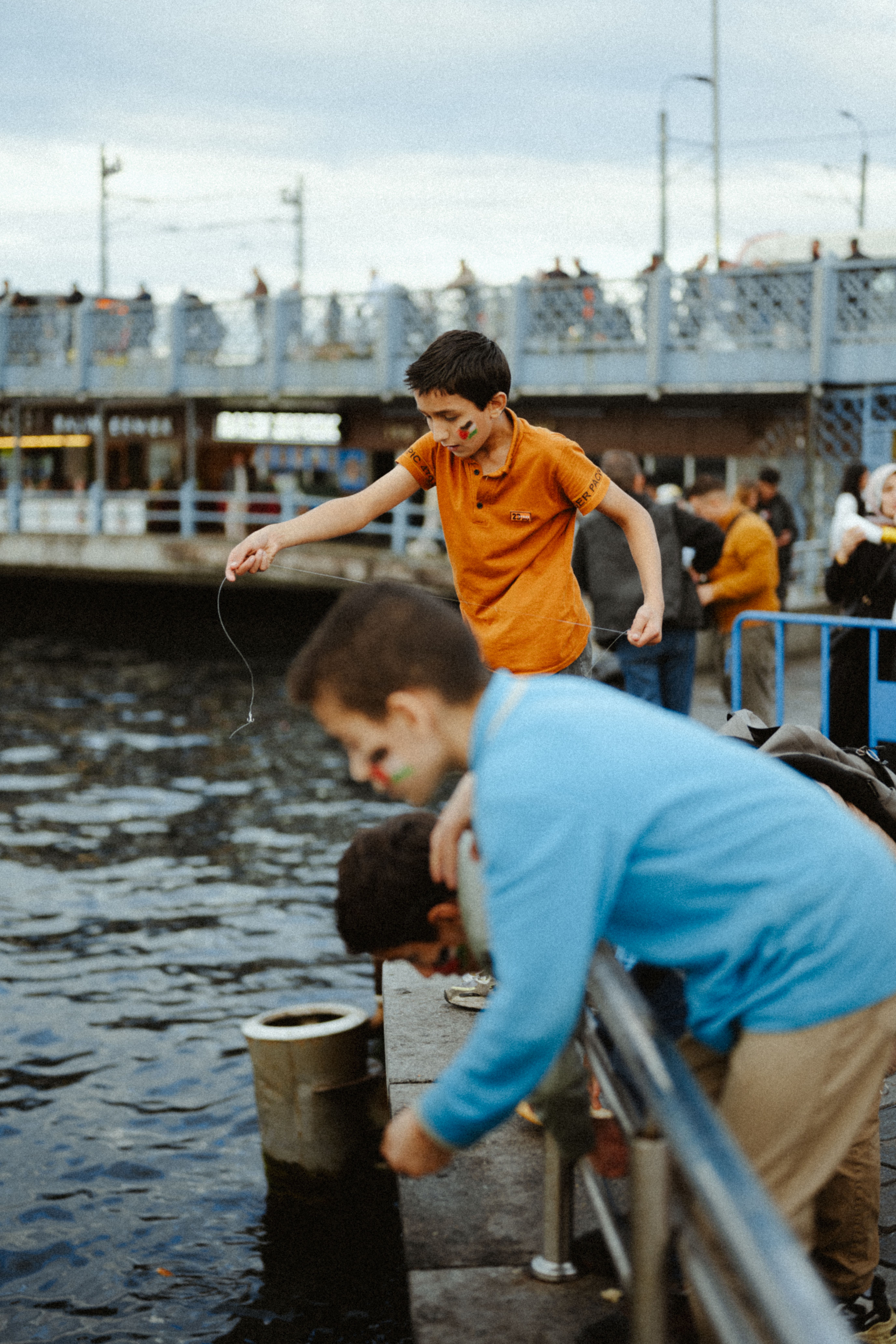 Candid shot of children fishing by the Galata Bridge, Istanbul, capturing a lively street scene.