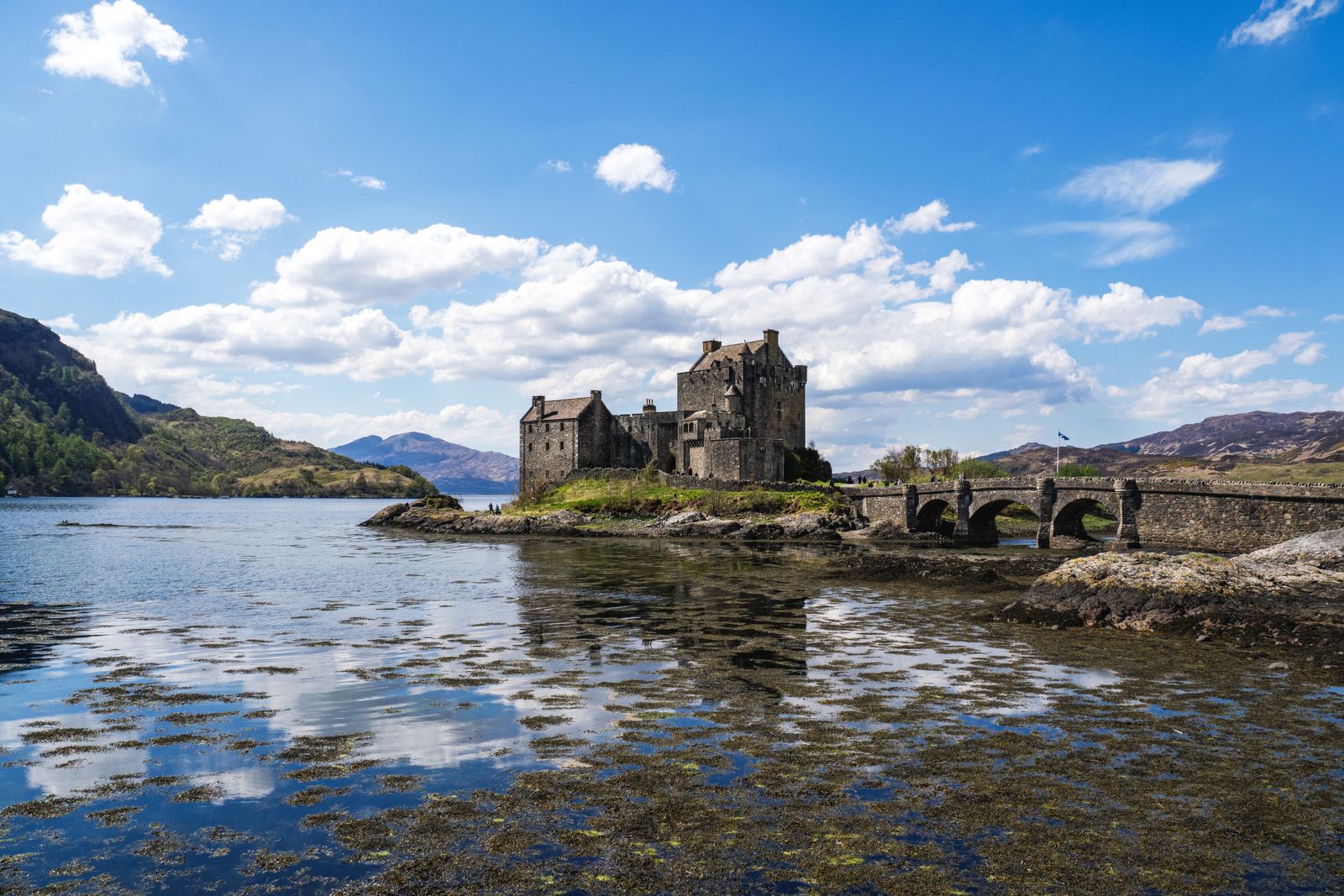 Eilean Donan Castle and its stone bridge reflected in Loch Duich under a blue sky