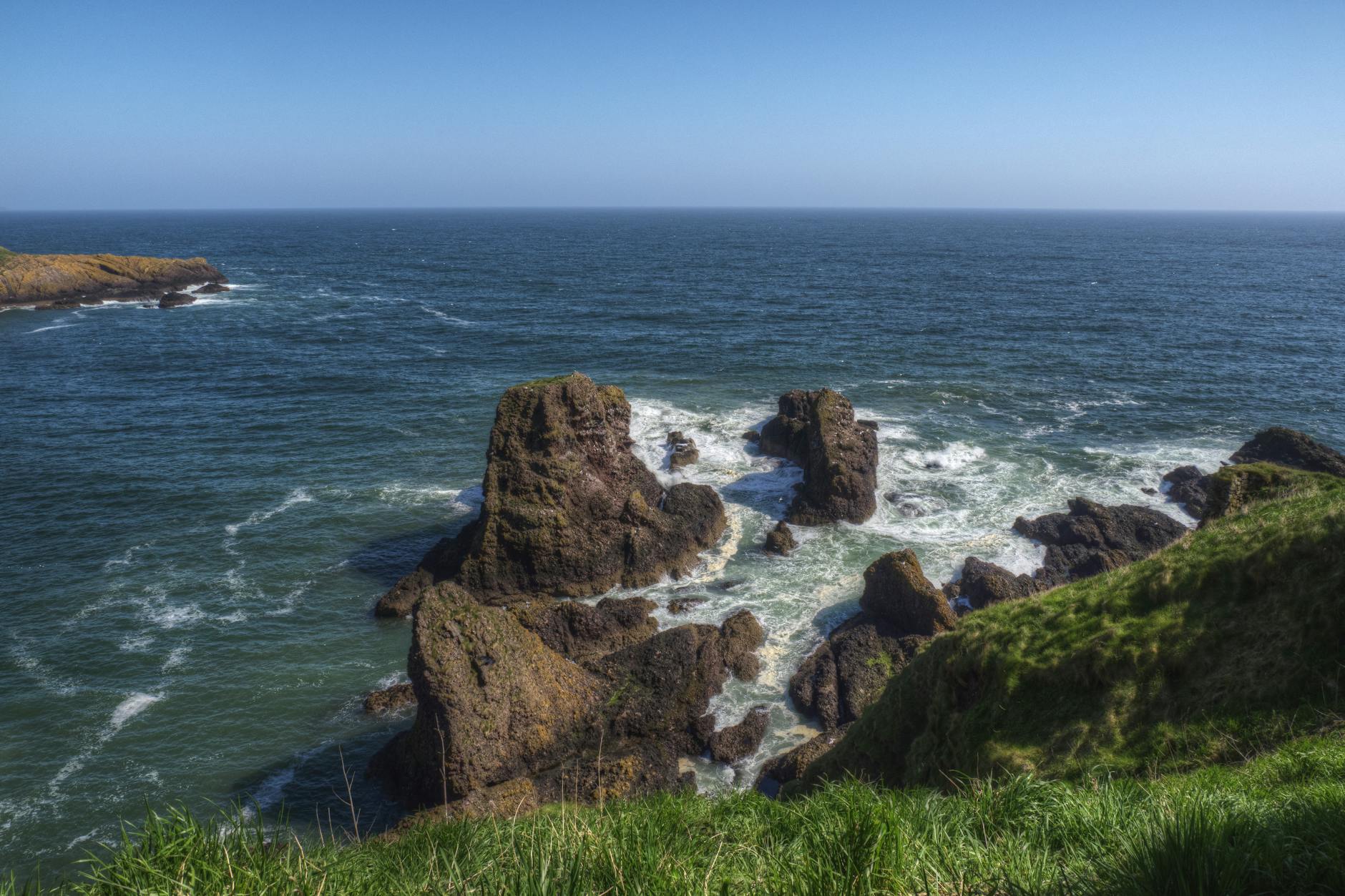 Stunning view of rocky coastal cliffs with vibrant blue ocean under clear sky.