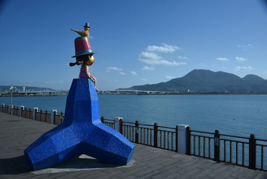 Vibrant sculpture at a waterfront promenade with mountain backdrop under clear sky.