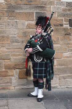 A Scottish bagpiper in traditional attire plays against a stone wall. Iconic cultural scene.