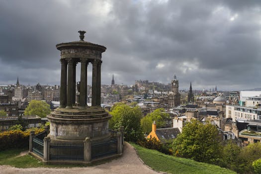 Panoramic view of Edinburgh city from Calton Hill with dramatic skies and lush greenery.