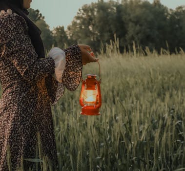 A serene scene with a woman holding a lantern in a grassy field during dusk, exuding a warm glow.