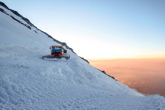 A snow groomer traversing a snowy Alpine mountain slope during a stunning sunset.