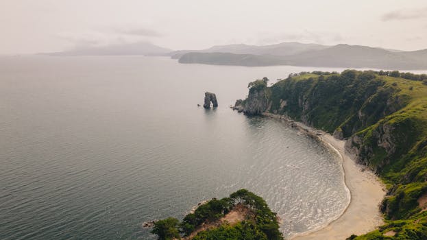 A stunning aerial shot of a coastal landscape featuring cliffs, serene waters, and lush greenery.