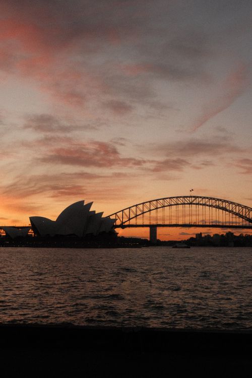 Free Scenic view of Sydney Opera House and Harbour Bridge during a vibrant sunset over the water. Stock Photo