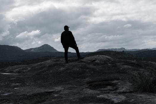 A lone hiker stands on a rocky hilltop in Bengaluru, enjoying the dramatic, cloudy landscape.