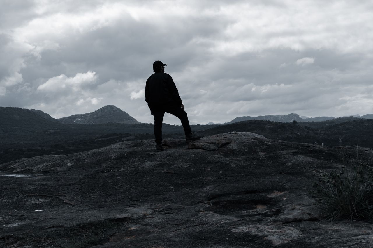 a lone hiker stands on a rocky hilltop in bengaluru enjoying the drama