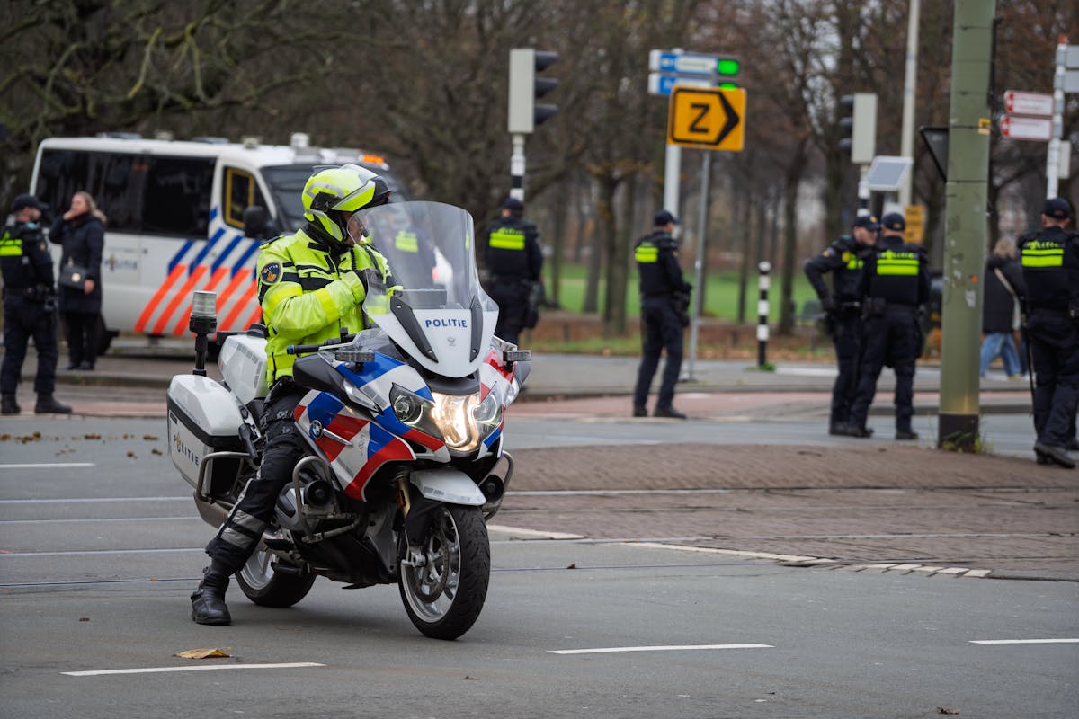 Officer on police motorcycle leading street surveillance, flanked by fellow officers.