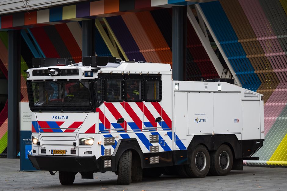 A Dutch police water cannon vehicle parked against a colorful urban backdrop.