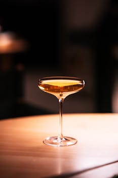 A sophisticated cocktail in a coupe glass on a wooden table, exuding a warm and inviting atmosphere.