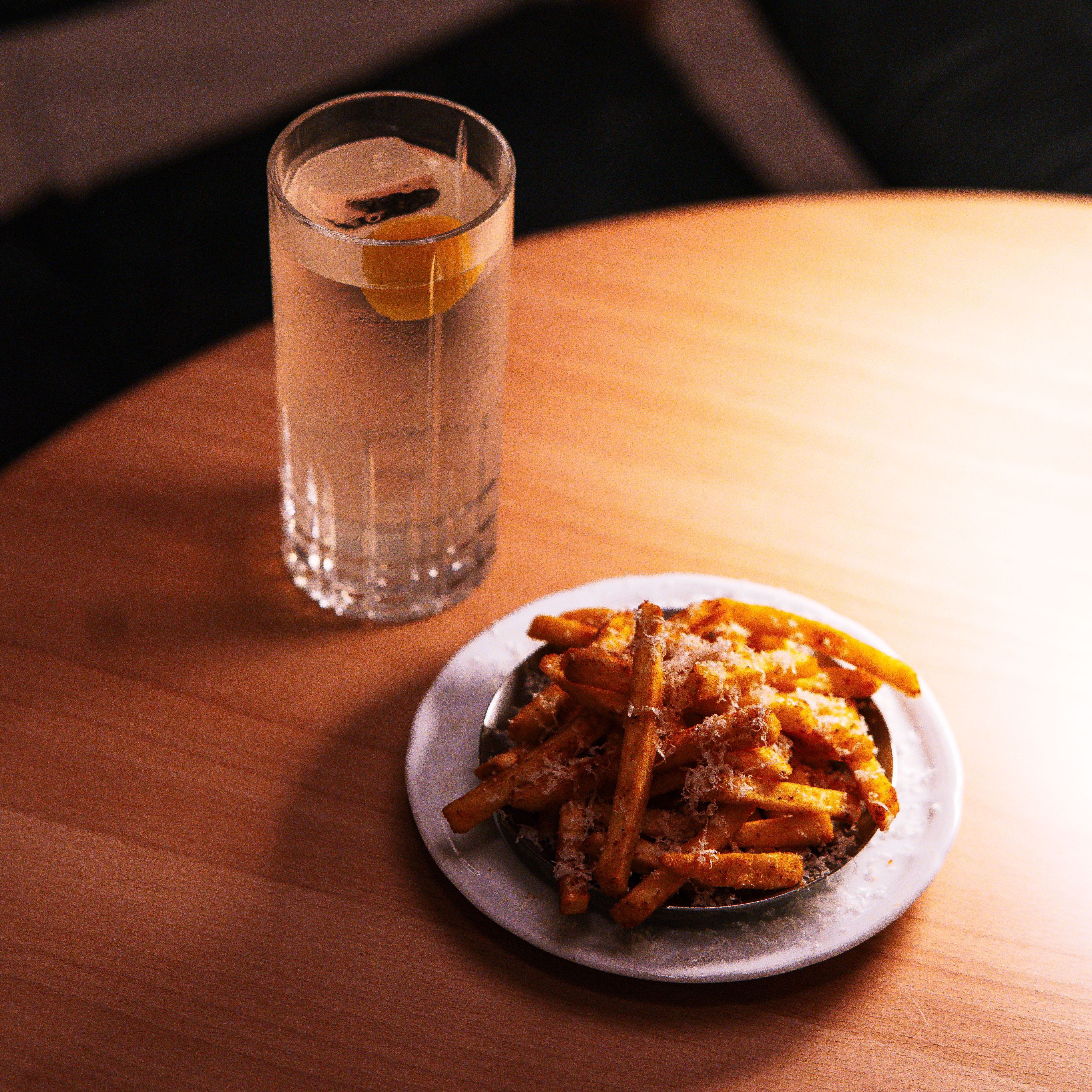 A plate of seasoned fries with a lemon-infused cocktail on a warm-lit wooden table, ideal for dining content.