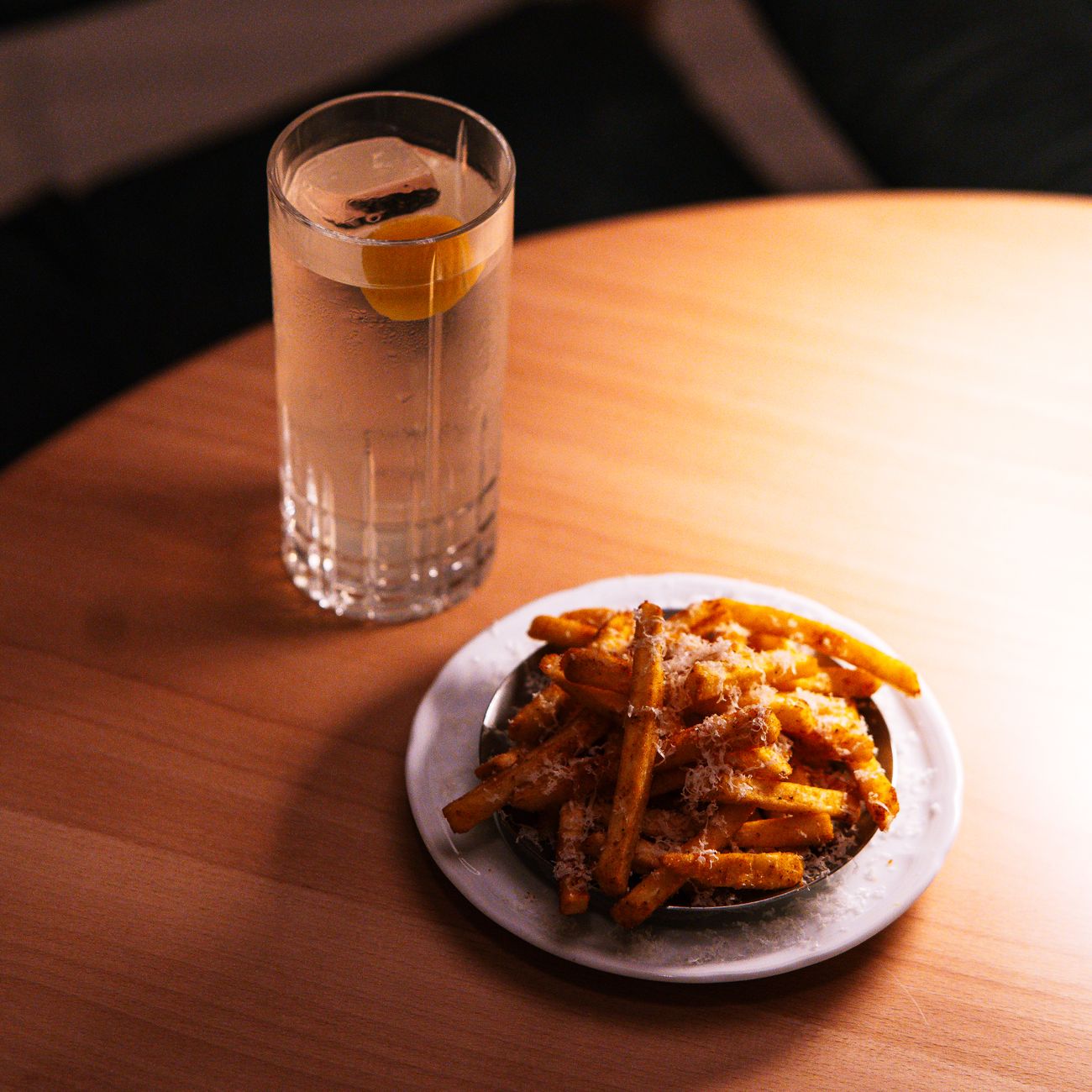 A plate of seasoned fries with a lemon-infused cocktail on a warm-lit wooden table, ideal for dining content.
