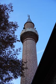 Towering minaret with intricate brick design reaching into a clear blue sky.