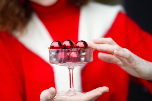A festive setup with red Christmas ornaments in a crystal glass, emphasizing holiday spirit.