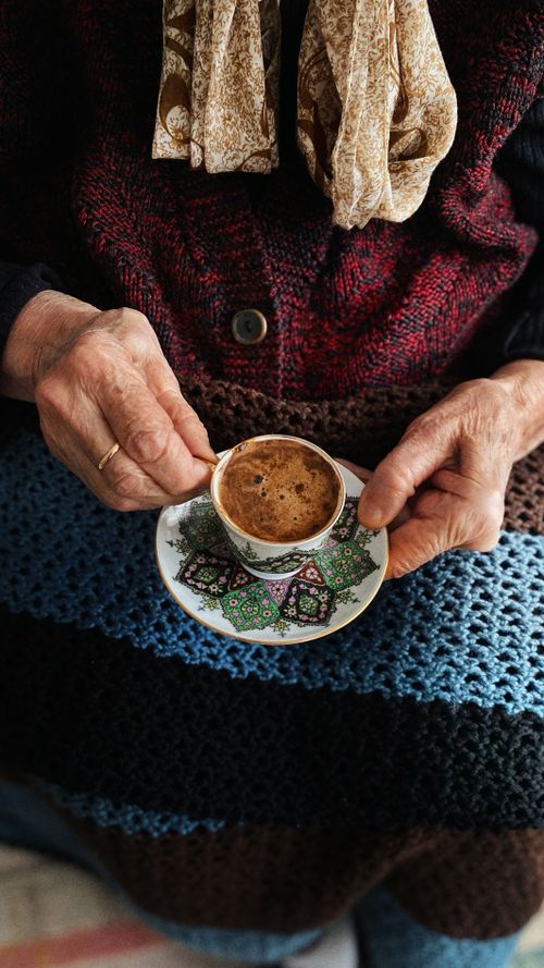Free Cozy scene of elderly hands gently gripping a decorated coffee cup with saucer. Stock Photo