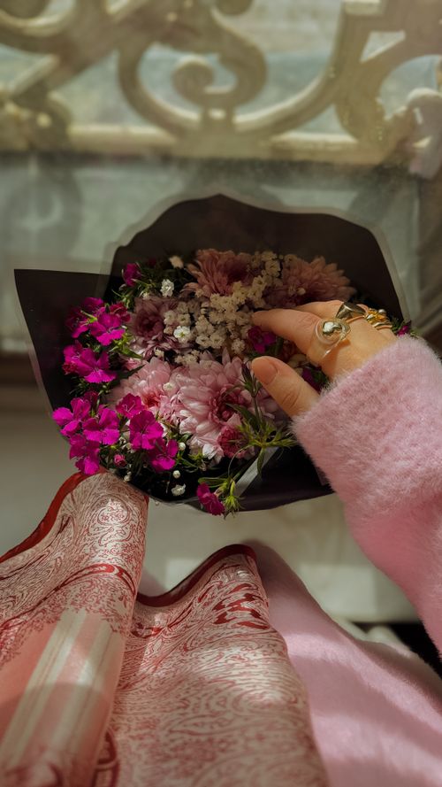 Free A delicate hand holding a vibrant floral bouquet with pink and white flowers, wrapped in intricate paper. Stock Photo