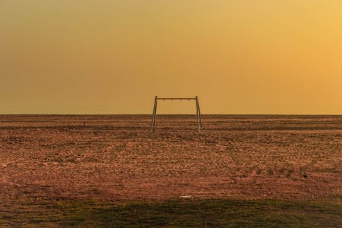 Free A solitary swing set stands in a vast, empty desert under a warm sunset sky. Stock Photo