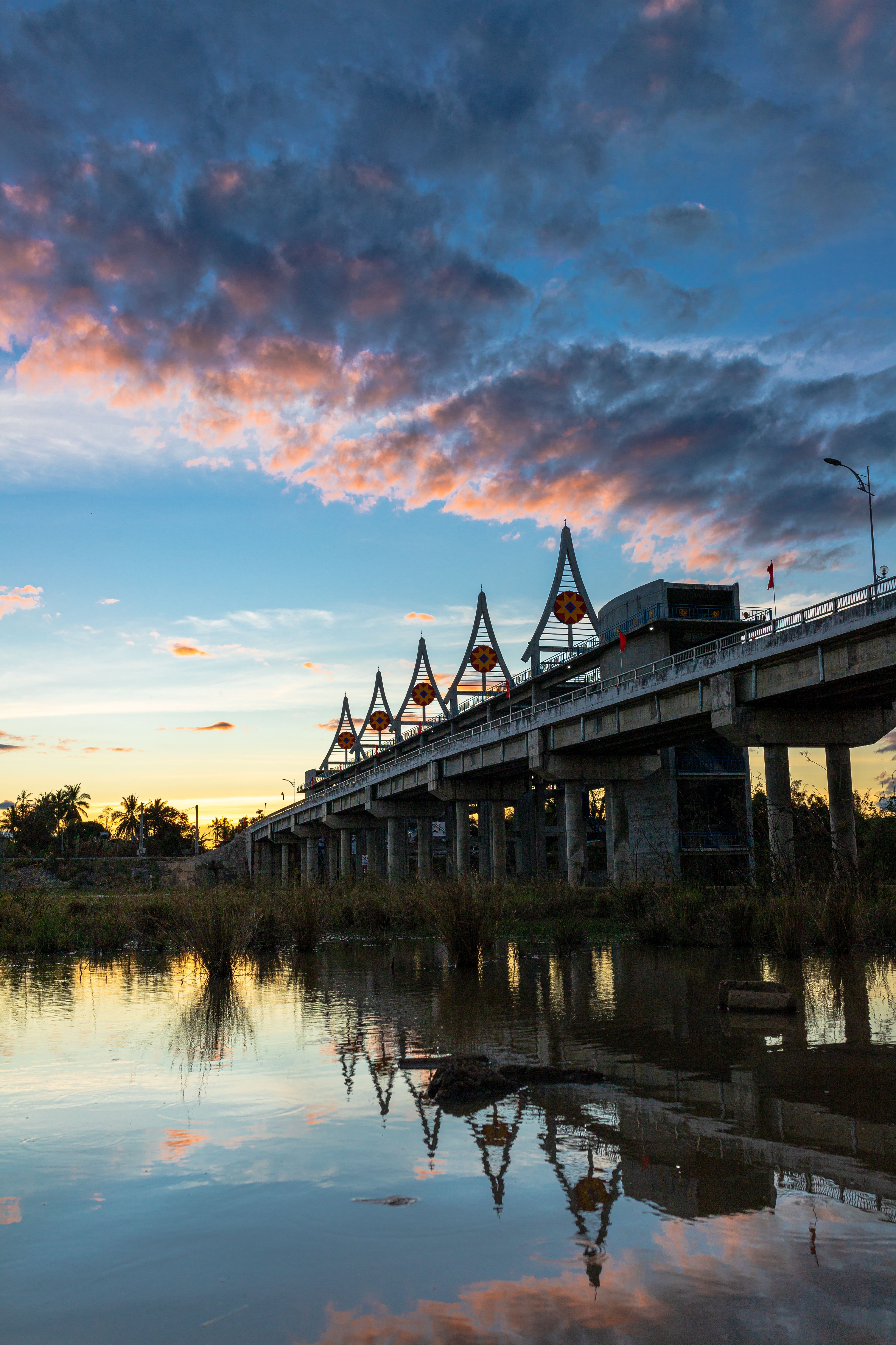 Sunset view of Bac Luan border area with river, bridge lights, travelers returning, poetic atmosphere, reflective water, warm golden sky, cinematic realistic travel photography, highly detailed