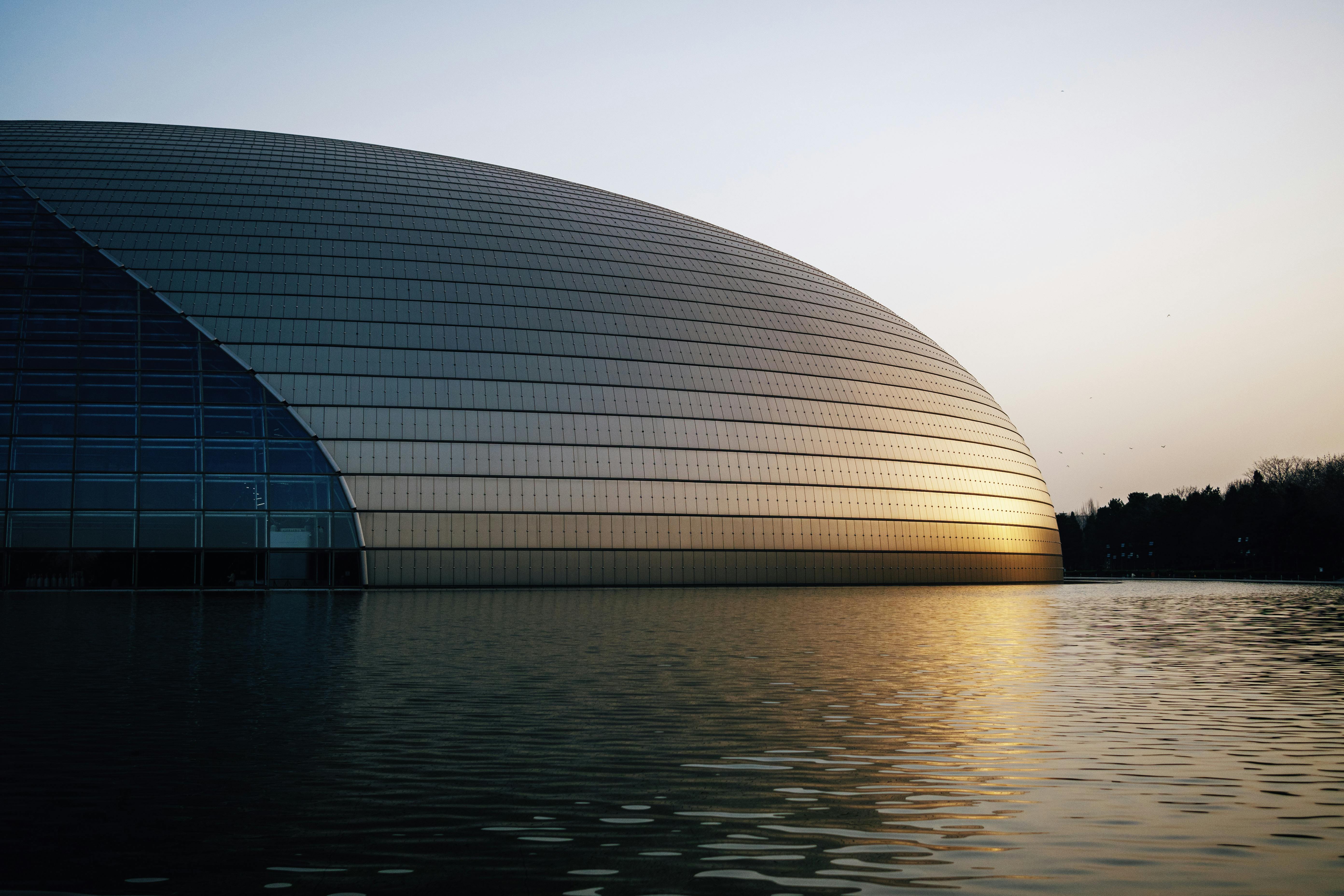 Elegant view of futuristic architectural landmark reflecting in water at sunset.