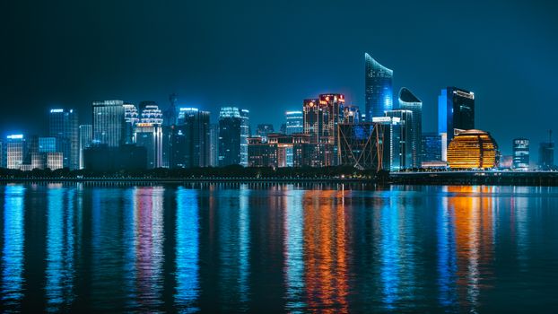 Vibrant night cityscape of Hangzhou reflecting in Qiantang River, showcasing modern skyscrapers.