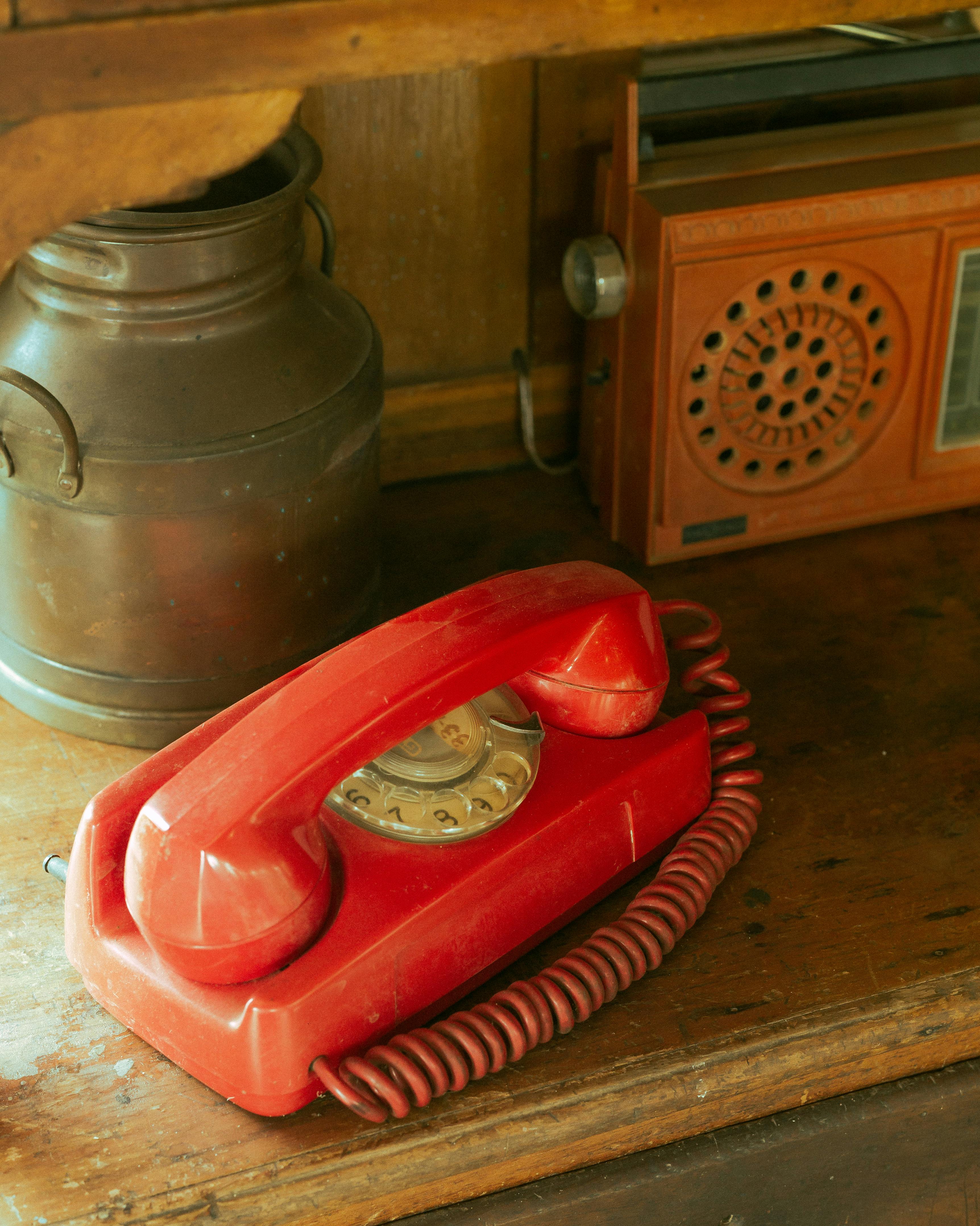 grátis Um telefone antigo de disco vermelho repousa em uma prateleira rústica de madeira, ao lado de uma decoração retrô, em São Paulo, Brasil. Foto profissional