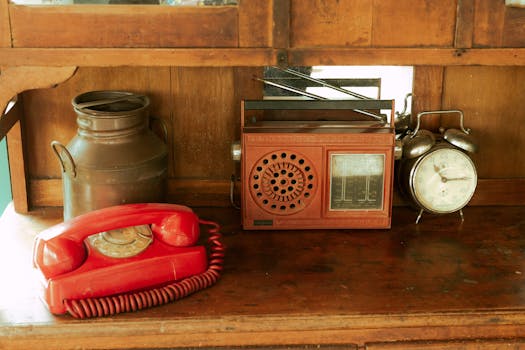 A vintage scene featuring a red rotary phone, old radio, and antique clock on a wooden shelf.