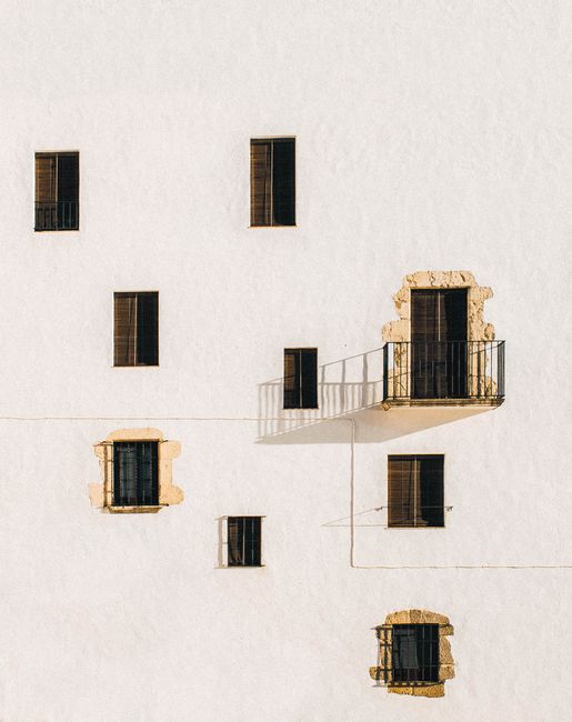 Minimalist architecture featuring a white wall with windows and shadows creating a dramatic effect.