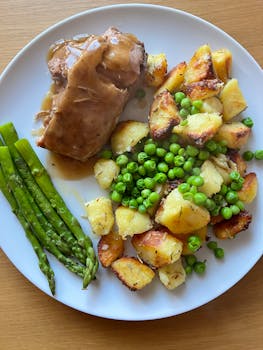 Roast pork with gravy, crispy potatoes, peas, and asparagus on a white plate.